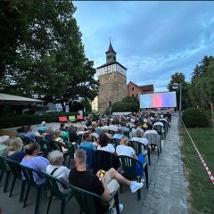 besetzte Stuhlreihen vor einer Leinwand auf der ein Film läuft im Freien