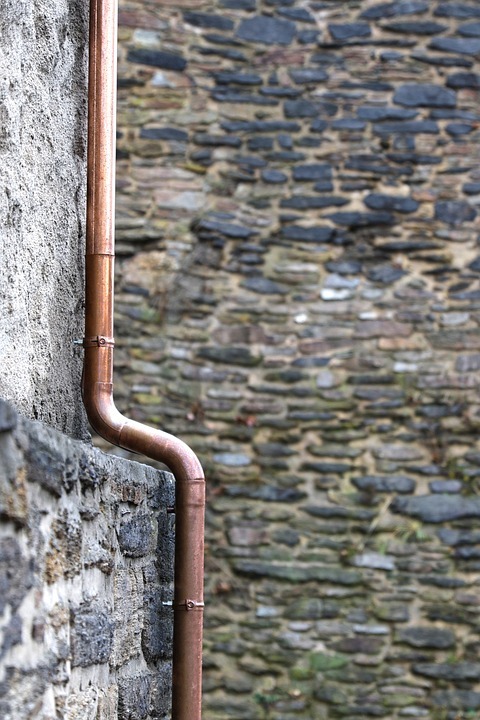 Kupferdachrinnen-Fallrohr an einer Steinmauer