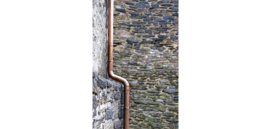Kupferdachrinnen-Fallrohr an einer Steinmauer