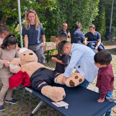 Das Bild zeigt wie Kinder an einer Mitmachstation einem sehr großen Teddy den Kopf und die Arme verbinden
