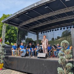 Das Bild zeigt Frau Bürgermeisterin Hannemann bei der Eröffnungsrede des Weibertreufest 2026 auf der Bühne im Hintergrund sitzt die Stadtkapelle mit Ihren Instrumenten auf Stühlen. Die Bühne ist mit Bäumchen und Blumen derkoriert.