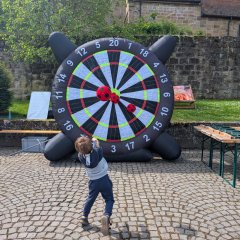 Das Bild zeigt eine Riesendartscheibe die mit Luft aufgeblasen ist und ein Kind das einen Klettball Richtung der Scheibe wirft.