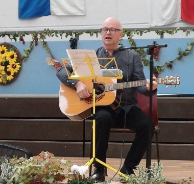 Auf der herbstlich geschmückten Bühne sitzt Pastor Wittenzellner und begleitet mit der Gitarre zum Lied „Die Gedanken sind frei".