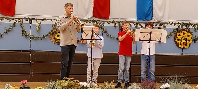 Drei Schüler und ein Lehrer der Städtischen Musikschule stehen auf einer Bühne und spielen Trompete.