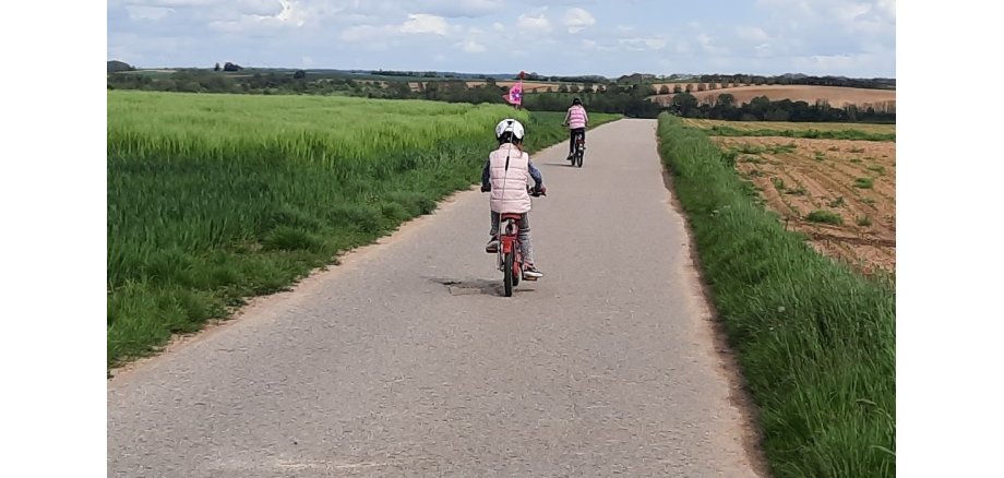 Feldweg mit 2 radelnden Kindern von hinten fotografiert