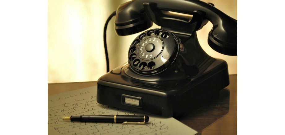 Altes Telefon mit Hörer und Wählscheibe in schwarz mit davor liegendem schwarzem Kugelschreiber
