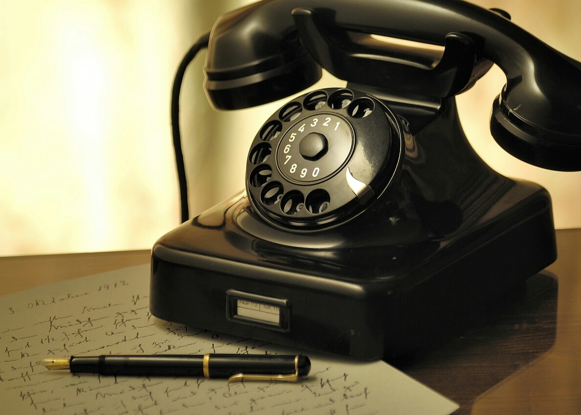 Altes Telefon mit Hörer und Wählscheibe in schwarz mit davor liegendem schwarzem Kugelschreiber